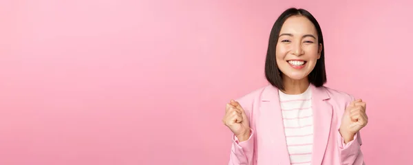Entusiasta commessa, asiatica donna aziendale dire di sì, raggiungere l'obiettivo e celebrare, trionfare, guardando con gioia e sorridente, in piedi su sfondo rosa — Foto Stock