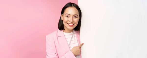 배를 향해 손가락 질하고, 빈 공간에서 핑크 색 배경 위에 옷을 입고 서 있는 일본 회사 여성 이 행복하게 미소짓는 모습 — 스톡 사진