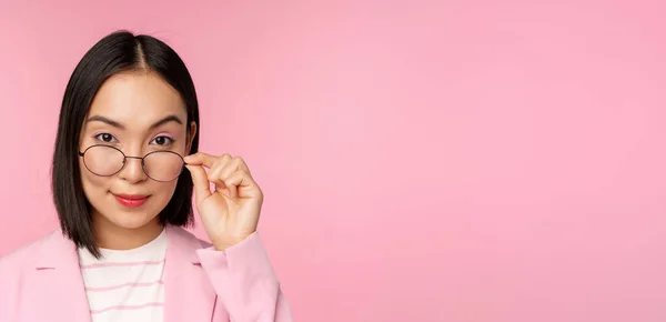 Ritratto di donna d'affari asiatica in occhiali, guardando incuriosito la macchina fotografica e sorridente, commessa professionale che fissa con interesse, sfondo rosa — Foto Stock