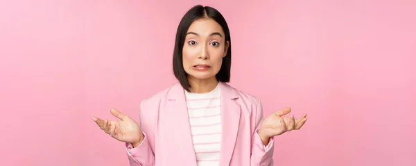 Retrato de mujer de negocios asiática confundida encogiéndose de hombros, buscando despistado y perplejo, no sé, no puedo decir, de pie sobre fondo rosa en traje de oficina —  Fotos de Stock