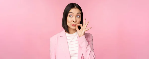 Portrait d'une femme d'affaires asiatique montrant un joint buccal, fermez les lèvres sur un geste clé, promettez de garder secret, debout sur un fond rose en costume — Photo