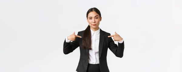 Professionele Aziatische zakenvrouw in pak wijzen op zichzelf als het aanbieden van de beste deals. Trots en zelfverzekerde verkoopster pronken, suggereren persoonlijke hulp of hulp, staande witte achtergrond — Stockfoto