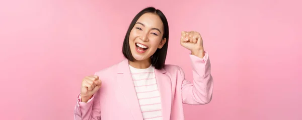 Nadšená asijská korporátní žena, podnikatelka zvedá ruku a jásá, triumfuje, vyhrává a slaví, stojí nad růžovým pozadím — Stock fotografie