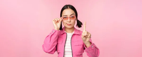 Imagen de chica asiática con cara seria, mostrando prohibir, regañar gesto, agitar el dedo señalando hacia arriba, expresar desaprobación, de pie sobre fondo rosa —  Fotos de Stock