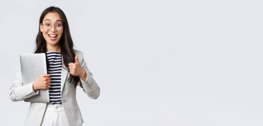 İş, finans ve istihdam, başarılı kadın girişimciler konsepti. Gözlüklü genç kendine güvenen iş kadını, baş parmak işareti yapıyor, dizüstü bilgisayarı tutuyor, en iyi hizmet kalitesini garanti ediyor.