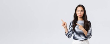 Yaşam tarzı, güzellik ve moda, insanların duygu konsepti. Hüzünlü Asyalı kız şikayet ediyor, pişmanlık duyuyor ya da kıskançlık duyuyor huzursuz bir şekilde somurtuyor ve reklam afişini işaret ediyor.