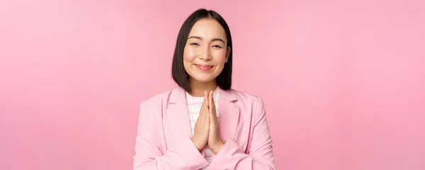 Dank u wel. Glimlachende Aziatische verkoopster, corporate dame in pak bedanken, hand in hand, dankbaarheid gebaar, staande over roze achtergrond — Stockfoto