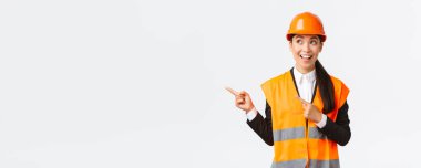 İnşaat, inşaat ve endüstriyel konsept. Heyecanlı ve ilgili Asyalı mimar, miğfer ve güvenlik kıyafetleri mühendisi ilginç bir projeye sol üst köşeden bakıyor.