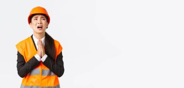 Umutsuz ve pervasız Asyalı kadın inşaat yöneticisi, mimar Tanrı 'ya yalvarıyor, güvenlik kaskı takıyor, dua ederken el ele tutuşuyor, yalvarıyor, Tanrı' dan yardım dileniyor, beyaz arka plan için yalvarıyor.