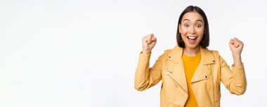 Asyalı bir kadın dans ediyor ve gülümsüyor, mutlu, zaferi kutluyor, zafer kazanıyor, beyaz arka planda duruyor.