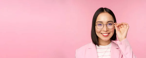 안경을 쓰고 웃으며 카메라 앞에 자신감 있게 서 있는 이시아 기업 여성의 사진을 클로즈업, 핑크 배경 — 스톡 사진