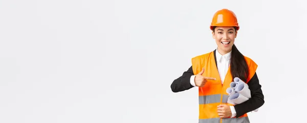 Professionelle selbstbewusste asiatische Architektin, Chefingenieurin in Schutzhelm zeigt mit dem Finger auf Baupläne, zeigt Projektplan oder Bauunterlagen, stehender weißer Hintergrund — Stockfoto