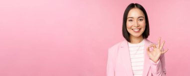 Harika iş, aferin sana. Gülümseyen Asyalı iş kadını tamam, tamam işareti, iyi iş, tavsiye şirketi, kendine güvenen profesyonel, pembe bir geçmiş