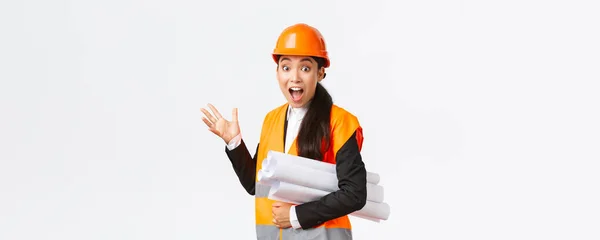 Impresionado y fascinado ingeniero asiático, arquitecto principal en el área de la construcción, apuntando hacia atrás en algo impresionante, llevar el plano del proyecto, con casco de seguridad y chaqueta reflectante — Foto de Stock