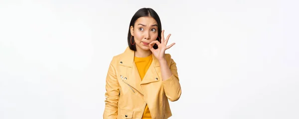 Image of young asian woman seal lips, silence gesture, zipping her mouth with promise, standing over white background — Stock Photo, Image