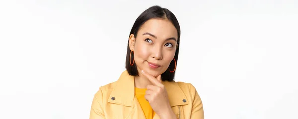 Primo piano di donna asiatica pensare, guardando verso l'alto premuroso, meditando smth con piacere sorridente faccia, in piedi su sfondo bianco — Foto Stock