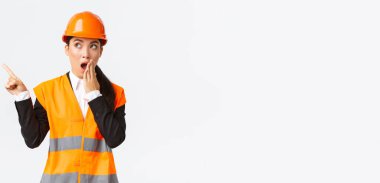 Şaşırmış ve etkilenmiş Asyalı kadın mühendis, güvenlik kaskı ve yansıtıcı ceketli inşaat müdürü, sol üst köşesinde nefes nefese kalmış parmak, hayrete düşmüş, ilginç bir şey buldu.