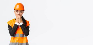 Endişeli ve endişeli Asyalı kadın mühendis inşaat alanında sorun yaşıyor, nefes darlığı çekiyor ve ağzını kapatıyor şok geçiriyor, kameraya paniklemiş bir ifadeyle bakıyor, güvenlik kaskı takıyor.