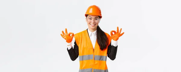 Ingénieur de construction asiatique confiante, chef d'entreprise montrant un geste correct après avoir mis un casque de sécurité, des lunettes et des gants avant d'entrer dans une zone dangereuse, fond blanc — Photo