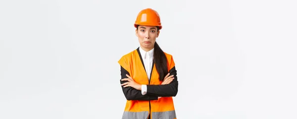 Kínos ázsiai női mérnök reflektív kabát, biztonsági sisak, keresztbe karok mellkas és önelégült meglepett, így buta hiba, jár természetes, álló fehér háttér — Stock Fotó
