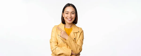 Portrét usměvavé asijské dívky ukazující prstem vlevo, zobrazující logo nebo kopírovací prostor, reklama na prázdné straně, stojící nad bílým pozadím — Stock fotografie