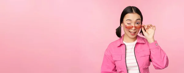 Anuncio de gafas. Elegante chica asiática moderna toca gafas de sol, viste de color rosa, posa contra el fondo del estudio. Copiar espacio — Foto de Stock