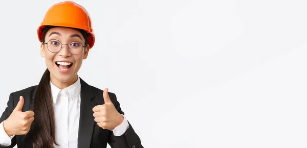 Izgatott boldog női ázsiai mérnök, építőipari vezető biztonsági sisak és üzleti öltöny mutatja hüvelykujj-up örvendezve, jóváhagyja a nagyon jó munkát, dicséret jól végzett munka, fehér háttér — Stock Fotó