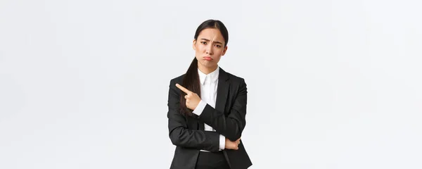 Missnöjd dyster asiatisk kvinnlig entreprenör förlorar, misslyckas jobb, står i kostym, surar och pekar finger vänster på misslyckande. Upprörd affärskvinna dela dåliga nyheter, vit bakgrund — Stockfoto