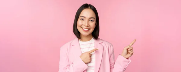 Enthusiastic professional businesswoman, saleswoman pointing fingers right, showing advertisement or company logo aside, posing over pink background — Stock Photo, Image