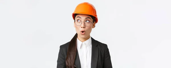 令人印象深刻的亚洲女首席建筑师、戴安全帽和西装的工业工程师的特写镜头，站在工厂的白色背景下，让人惊讶而惊讶 — 图库照片