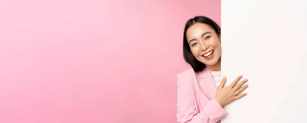 Portret van jonge Japanse zakenvrouw, corporate lady in pak wijst op muur met grafiek, toont diagram of advertentie op lege kopieerruimte, roze achtergrond — Stockfoto