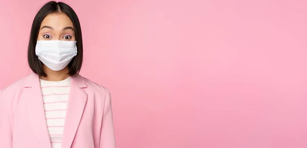 Retrato de mulher de negócios asiática em máscara facial médica, vestindo terno, conceito de trabalho de escritório durante a pandemia covid-19, de pé sobre fundo rosa — Fotografia de Stock