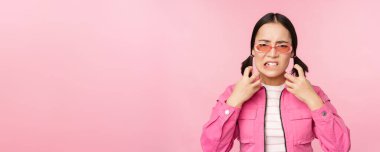 Image of angry, pissed off korean adult female model, shaking fists and shouting, screaming outraged, standing over pink background