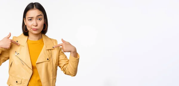 Imagem de unamused menina asiática apontando para si mesma, olhando com descrença cético para a câmera, posando contra fundo branco — Fotografia de Stock