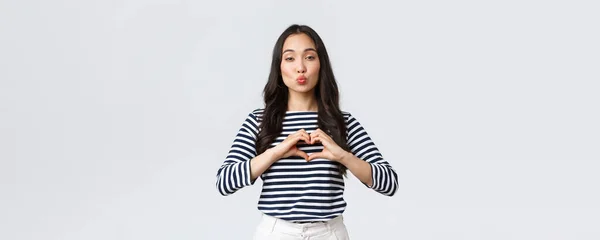Lifestyle, people emotions and casual concept. Lovely smiling adorable asian woman showing heart sign and smiling, express sympathy or care, sending air kiss at camera, standing white background — Stock Photo, Image