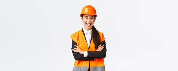Erfolgreiche lächelnde asiatische Ingenieurin, Architektin mit Schutzhelm, Jacke, verschränkten Armen und unbeschwertem Lachen, stellt Baupläne vor, zeigt Projekt, verkauft Häuser, weißer Hintergrund — Stockfoto