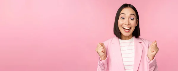 Lelkes eladónő, ázsiai vállalati nő igent mond, eléri a célt és ünnepel, diadalmaskodik, örül és mosolyog, áll a rózsaszín háttér felett — Stock Fotó