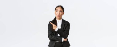 Etkileyici Asyalı bayan menajer, takım elbiseli iş kadını sol üst köşeyi işaret ediyor ve bakıyor.