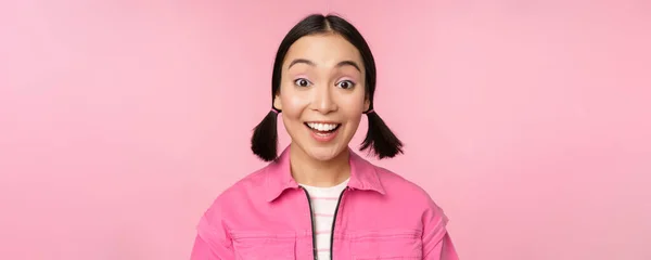 Primer plano retrato de hermosa chica asiática mirando entusiasta y sonriente, riendo y sonriendo, de pie feliz sobre fondo rosa — Foto de Stock