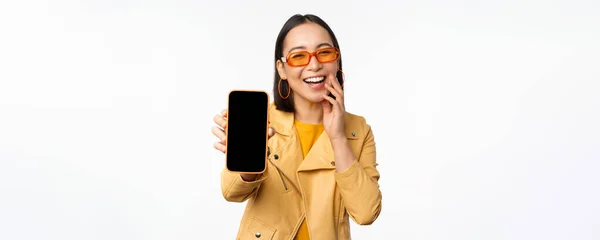 Entusiástico asiático modelo feminino, mostrando interface de aplicativo de smartphone, loja online ou site na tela do telefone móvel, de pé sobre fundo branco — Fotografia de Stock