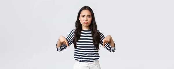 Estilo de vida, beleza e moda, as pessoas emoções conceito. Desapontado chateado jovem asiático mulher amuado e franzindo a testa descontente, apontando os dedos para baixo como reclamando sobre o produto ou serviço — Fotografia de Stock