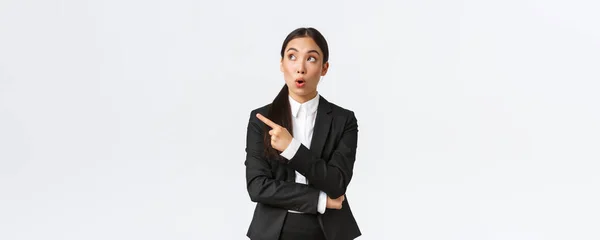 Beeindruckte hübsche asiatische Managerin, Geschäftsfrau im Anzug, die mit erstauntem Gesichtsausdruck nach links oben schaut, vor weißem Hintergrund stehend — Stockfoto