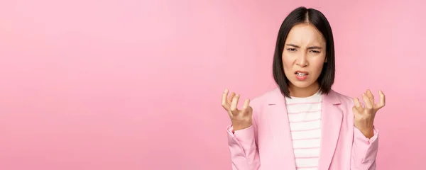 Retrato de mujer asiática enojada en traje, apretando puños y mirando furioso, indignado de smth malo, de pie sobre fondo rosa — Foto de Stock
