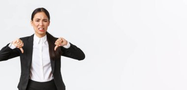 Hayal kırıklığına uğramış, kuşkucu ve üzgün Asyalı satıcı kadın kötü ürün ya da servisten şikayetçi, baş parmağını aşağı gösteren, hoşnutsuz, tatmin olmayan beyaz arka planda duran