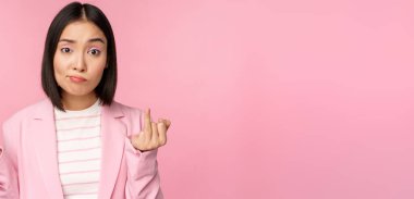 Asyalı genç bir iş kadını portresi, omuzlarını silkmiş, kafası karışmış, saf, pembe arka planda duran bir kadın.