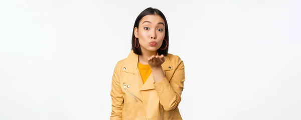 Cute korean stylish girl, sending air kiss, blowing mwah and looking silly romantic at camera, standing over white background — Stock Photo, Image