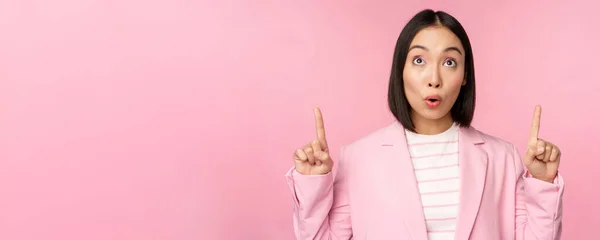 熱狂的な企業の労働者、指を指しているアジアのビジネス女性と笑顔、広告、ロゴ、ピンクの背景の上に立って示す — ストック写真