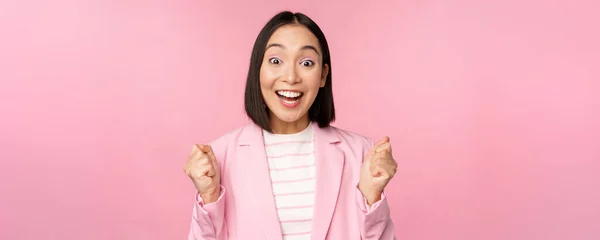 Entusiasta vendedora, mulher corporativa asiática dizer sim, alcançar o objetivo e celebrar, triunfar, olhando com alegria e sorrindo, de pé sobre fundo rosa — Fotografia de Stock