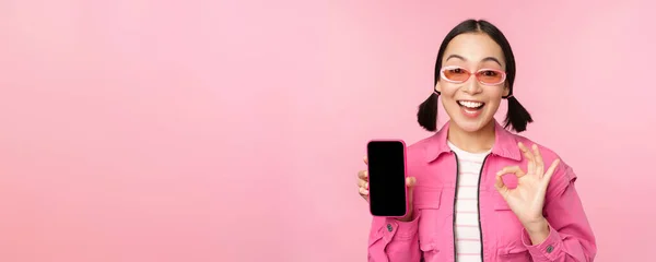 Entusiasta giovane donna asiatica mostrando ok, ok segno, sorridente soddisfatto, schermo del telefono cellulare, applicazione smartphone, in piedi su sfondo rosa — Foto Stock