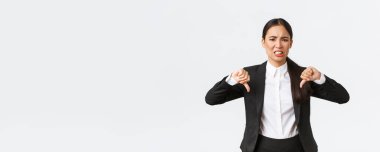 Hayal kırıklığına uğramış, kuşkucu ve üzgün Asyalı satıcı kadın kötü ürün ya da servisten şikayetçi, baş parmağını aşağı gösteren, hoşnutsuz, tatmin olmayan beyaz arka planda duran